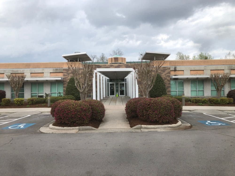 Modern building entrance with landscaped parking lot and accessible spaces. Cloudy sky.