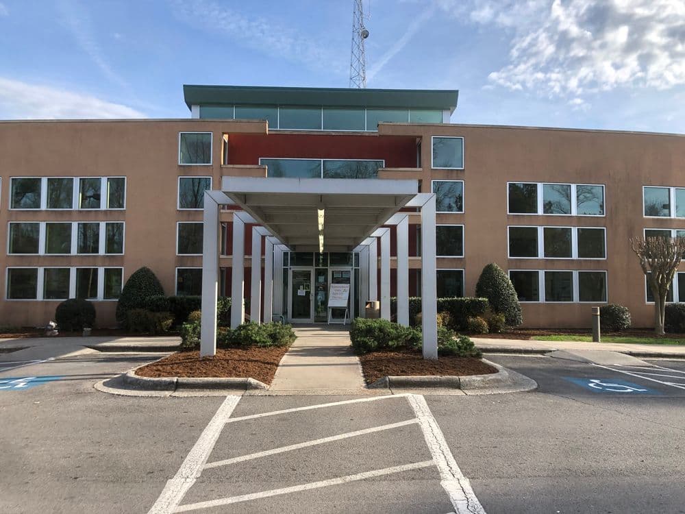 Modern office building entrance with large windows and accessible parking spaces.
