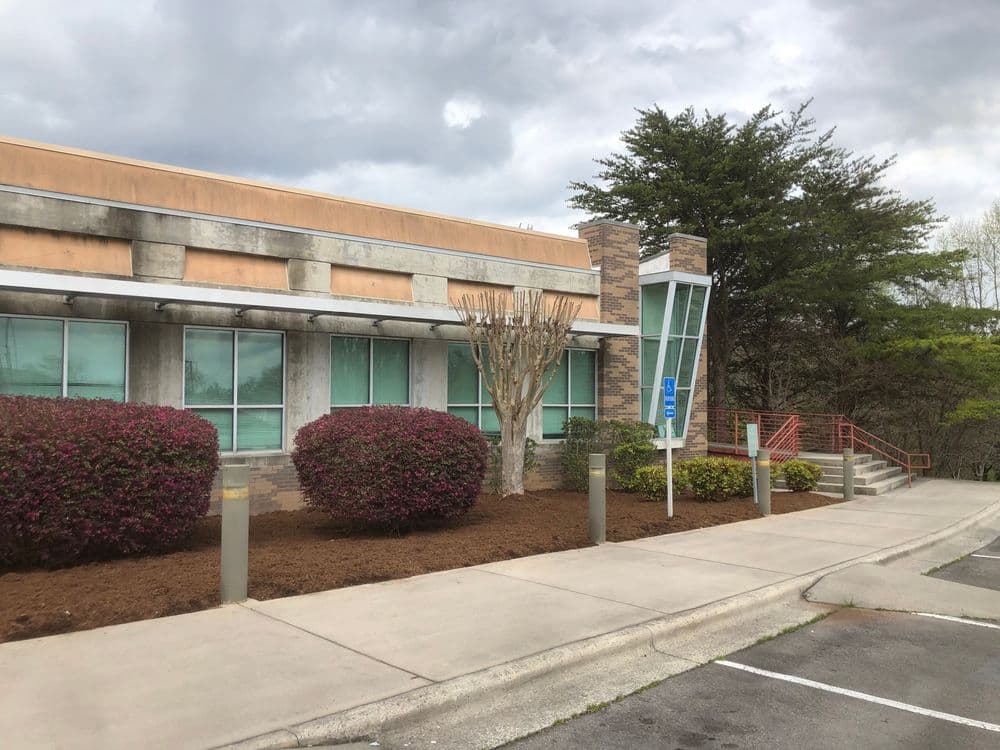 Modern building exterior with landscaped shrubs and accessibility ramp under a cloudy sky.