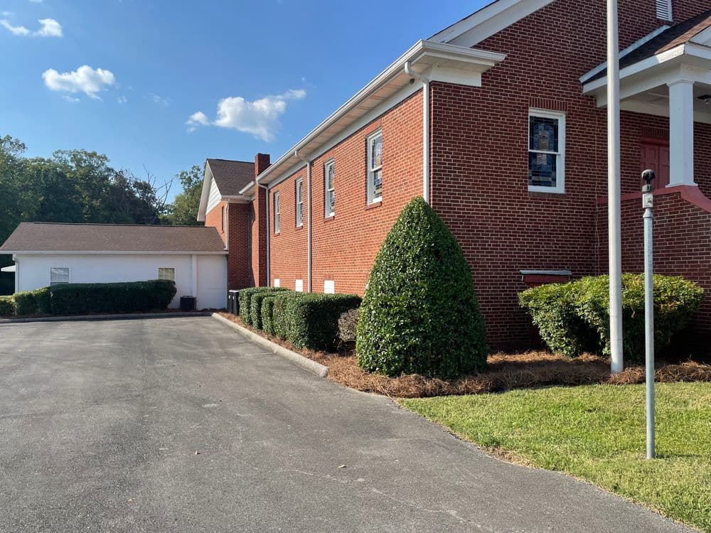 Red brick building with manicured hedges, driveway, and clear blue sky in the background.