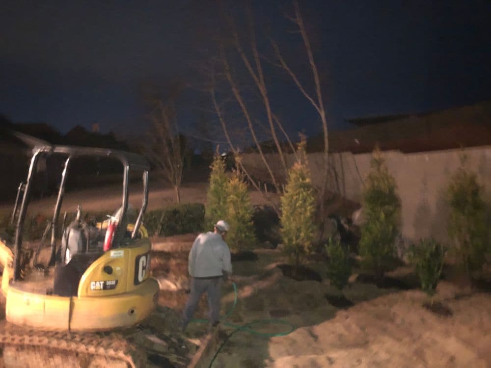 Construction worker using a CAT excavator to landscape a yard at night.