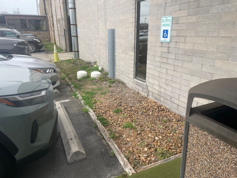 Landscape with gravel, accessible parking sign, and neighboring parked cars near a building.