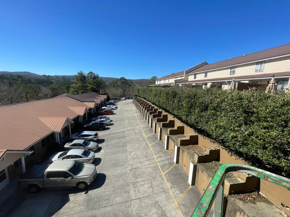 View of parking area with cars and townhomes under clear blue sky in residential complex.