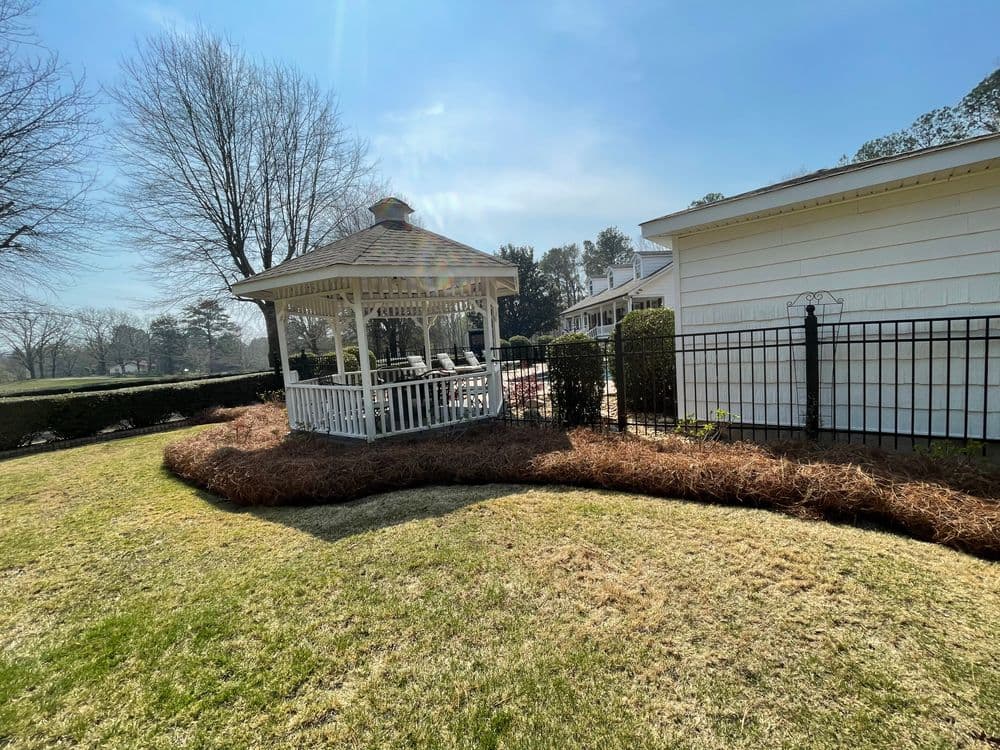 gazebo in garden with manicured lawn, fence, and trees under a clear blue sky