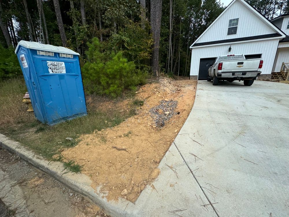 Construction site with portable toilet and gravel near a newly built house and driveway.