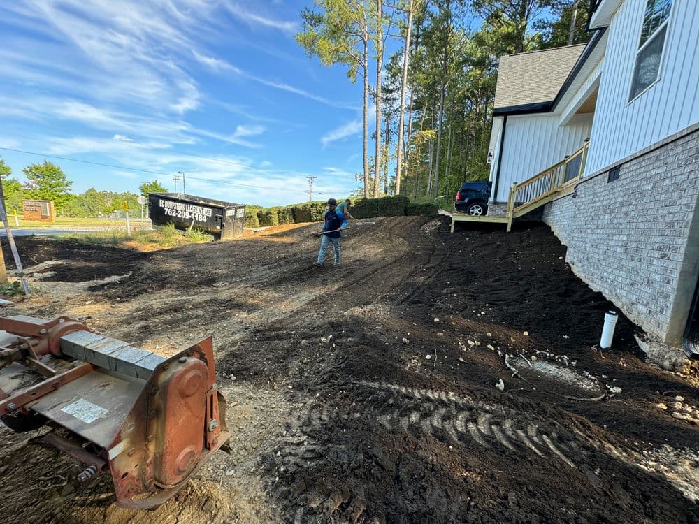 Landscaping project in progress at a home, featuring soil preparation and machinery on site.