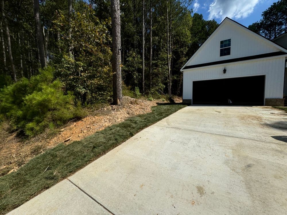 Newly landscaped driveway beside a modern home, surrounded by tall trees and green grass.
