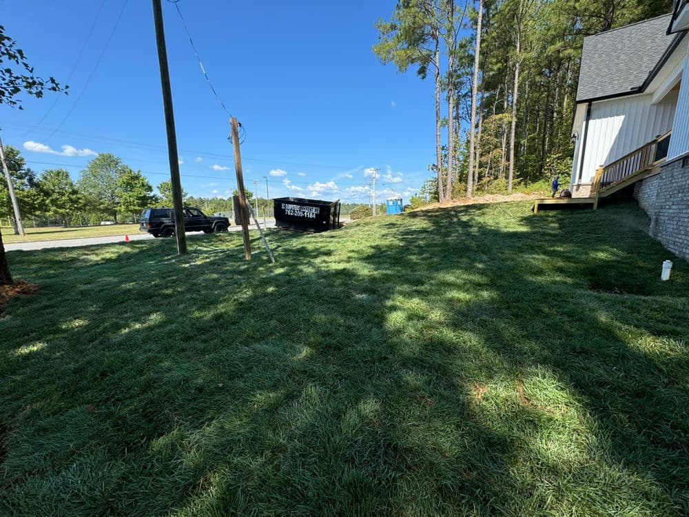 Construction site with new grass, dumpster, and tools near a house under blue sky.