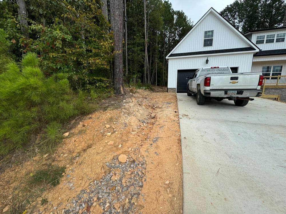 New house driveway with a white truck parked, surrounded by trees and gravel.