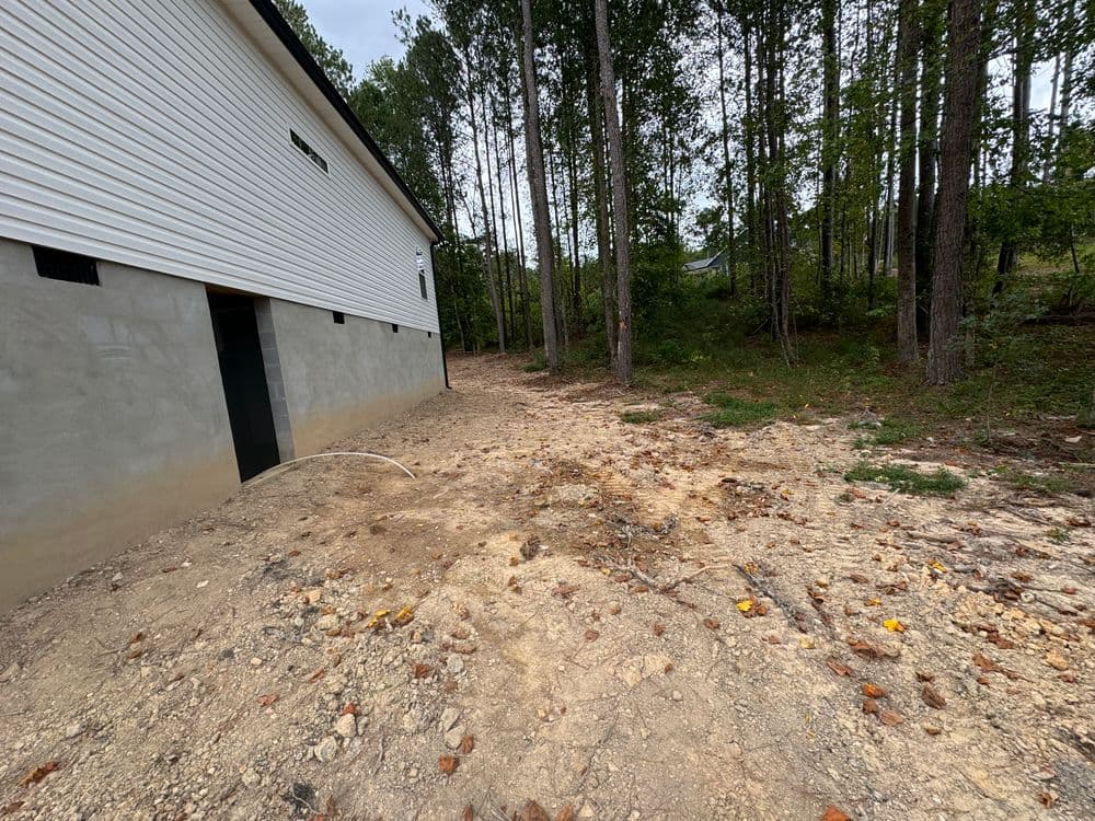 Exterior view of a house foundation with cleared land and surrounding trees.