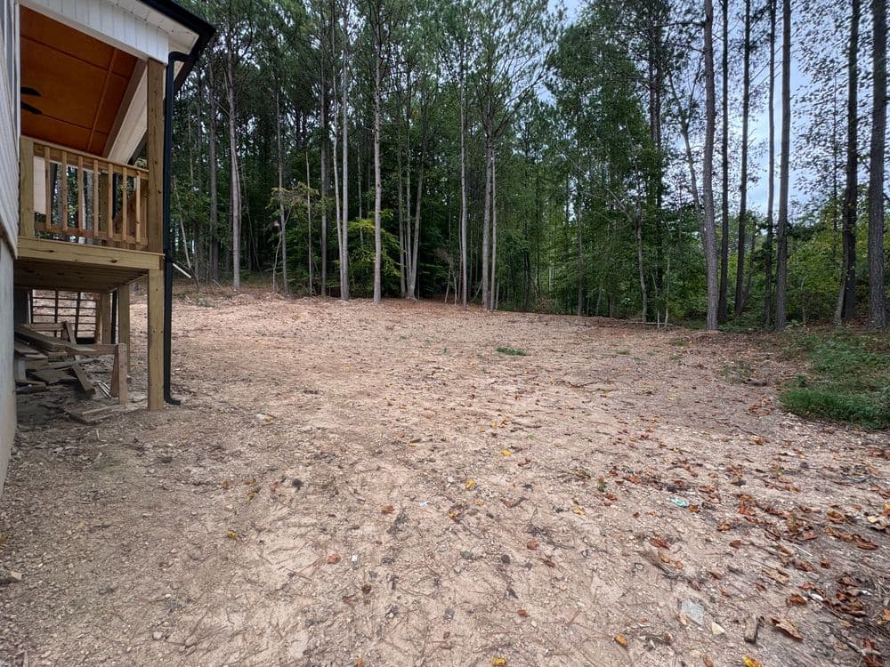 Cleared plot of land beside a house, surrounded by trees in a wooded area.