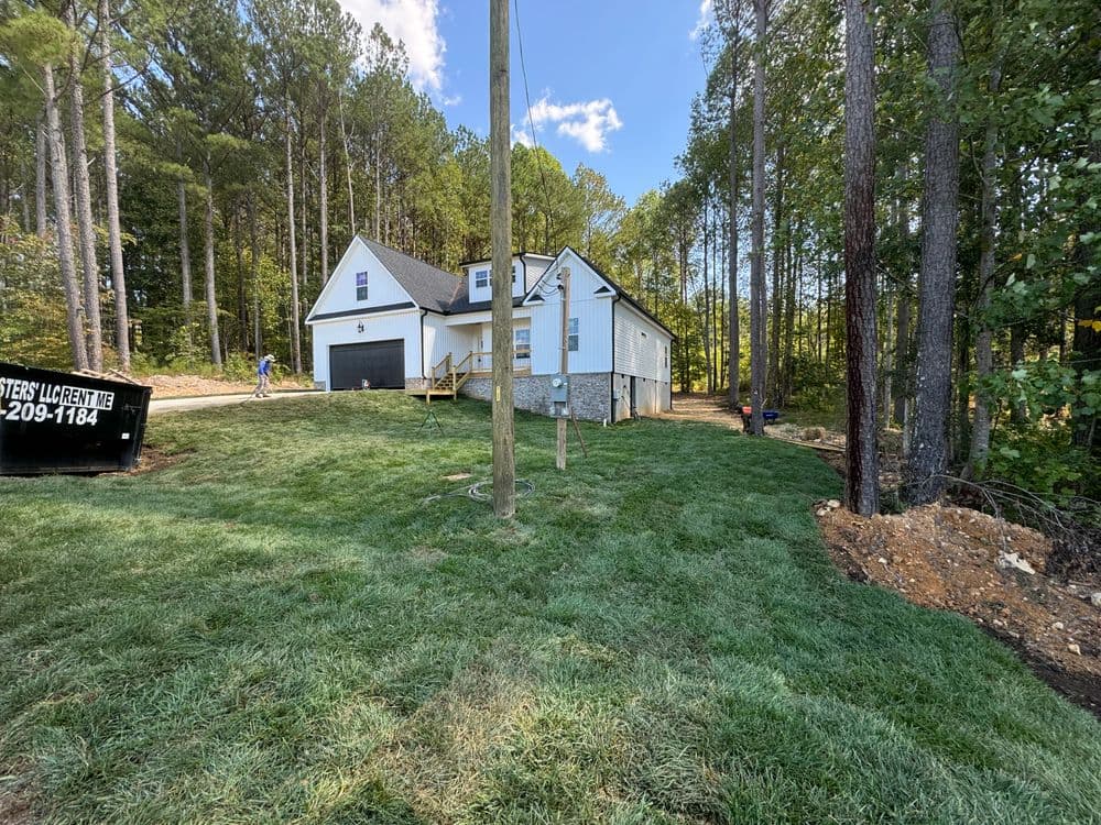 Modern two-story house surrounded by lush greenery and tall trees, with freshly landscaped yard.