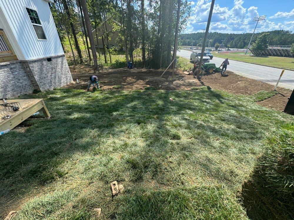 Landscaping project in progress with workers planting grass near newly constructed home.