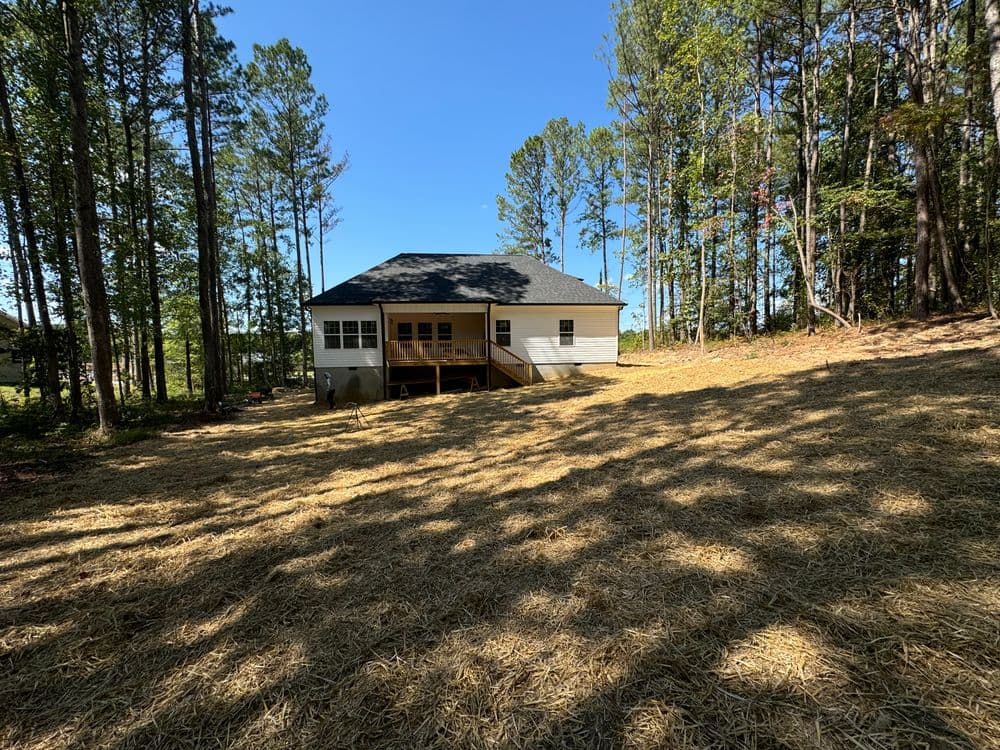 Newly built house surrounded by trees and a clear blue sky, featuring a spacious deck.
