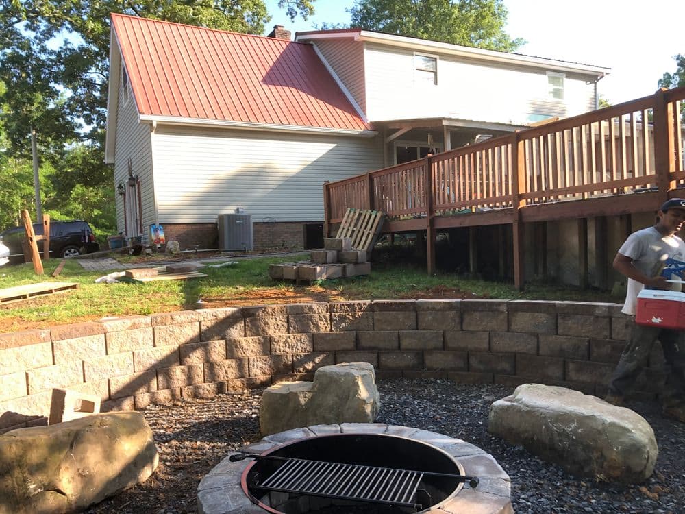 Backyard with fire pit, stone seating, and wooden deck on a house under renovation.