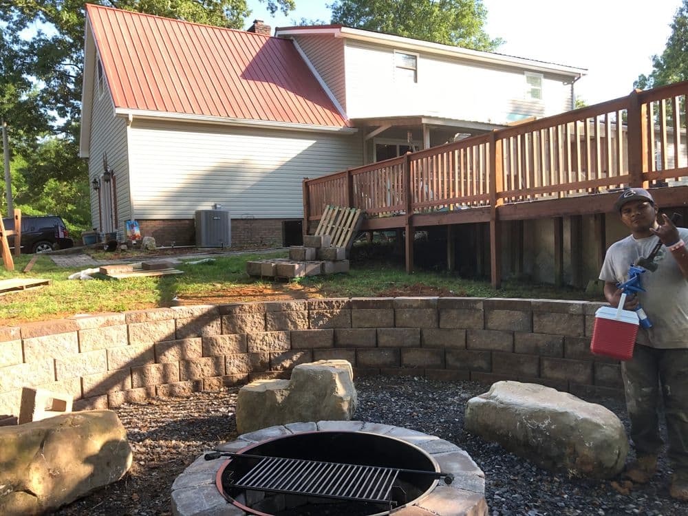 Backyard patio with a fire pit, picnic cooler, and a person in front of a house.