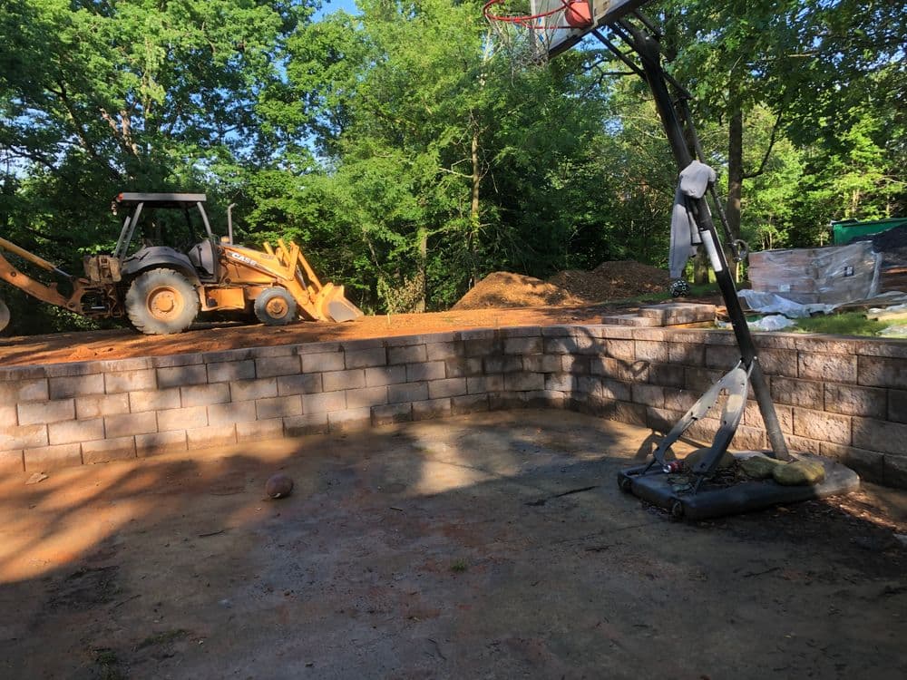 Construction site with a basketball hoop, tractor, and stacked materials in a wooded area.
