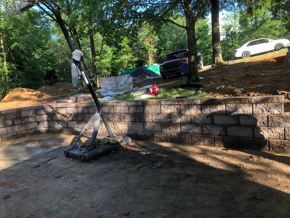 Construction site with a stone wall, landscaping materials, and machinery in a green area.