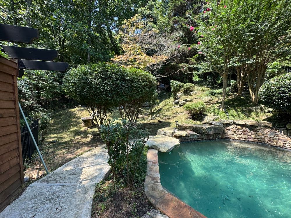 Lush garden with a stone pool surrounded by greenery and trees. Ideal backyard oasis.